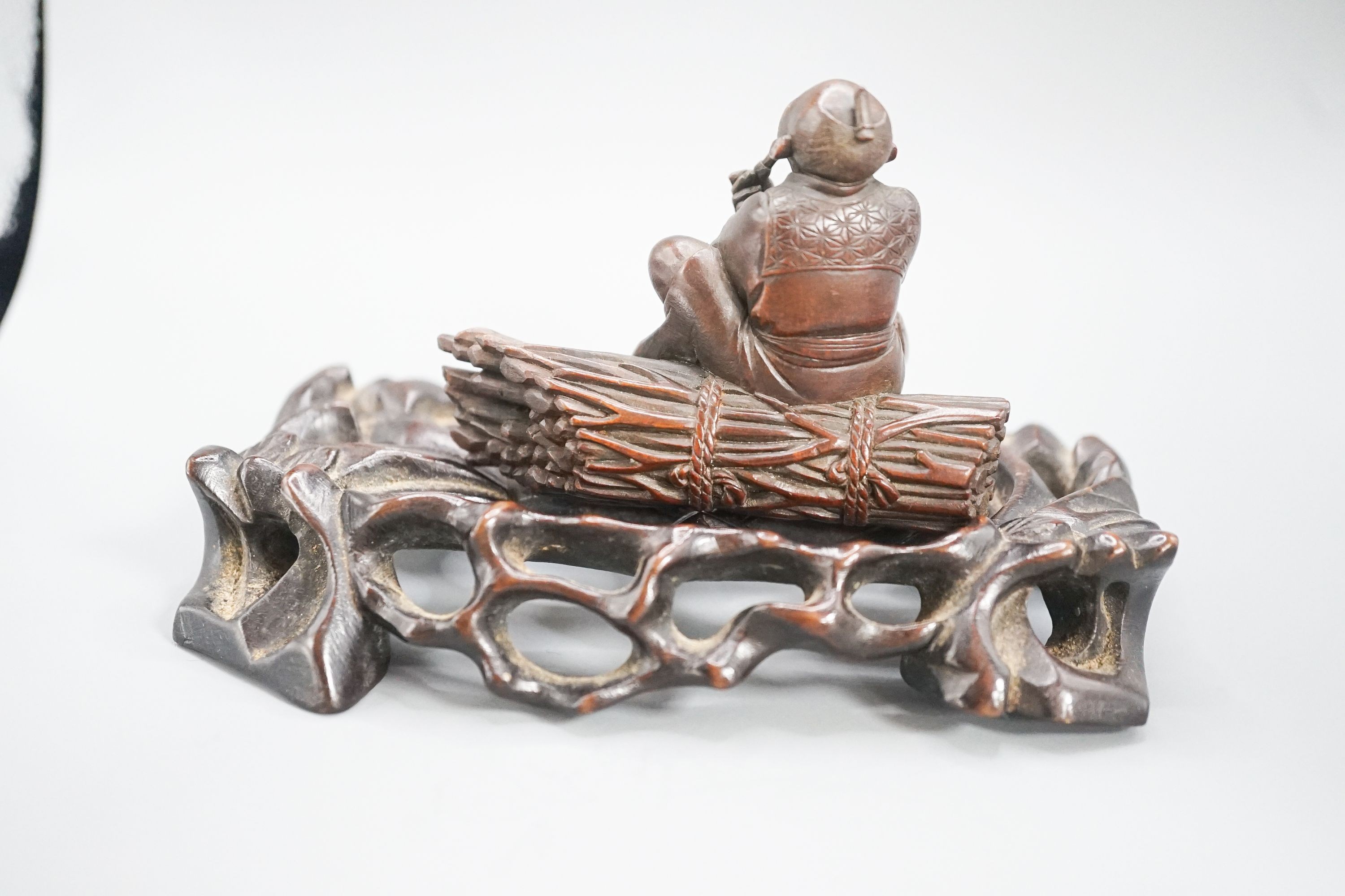 A 19th century Japanese wood okimono of a seated man smoking a pipe, signed, 7.8cm on a later hardwood stand